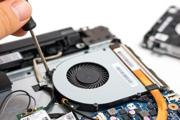 A close-up of a hand using a screwdriver to fix a laptop's internal fan.